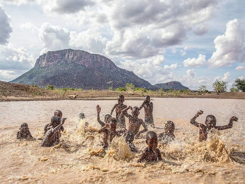 Group of kids bathing in rain water with Mt. Ololokwe in the background