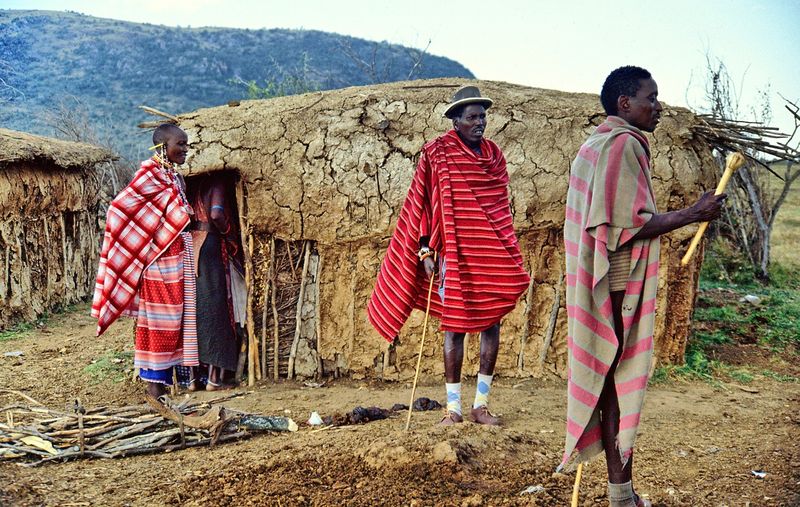 Maasai men and a woman in front of a traditional Maasai home